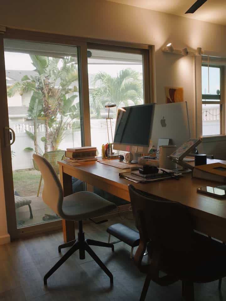 Natural toned home office featuring a wooden desk, computer setup, comfortable chairs, and a footrest under the desk