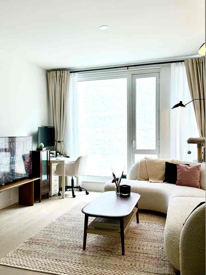 Bright white-toned living room featuring a soft curved sofa, wooden coffee table, and a home office space by the window