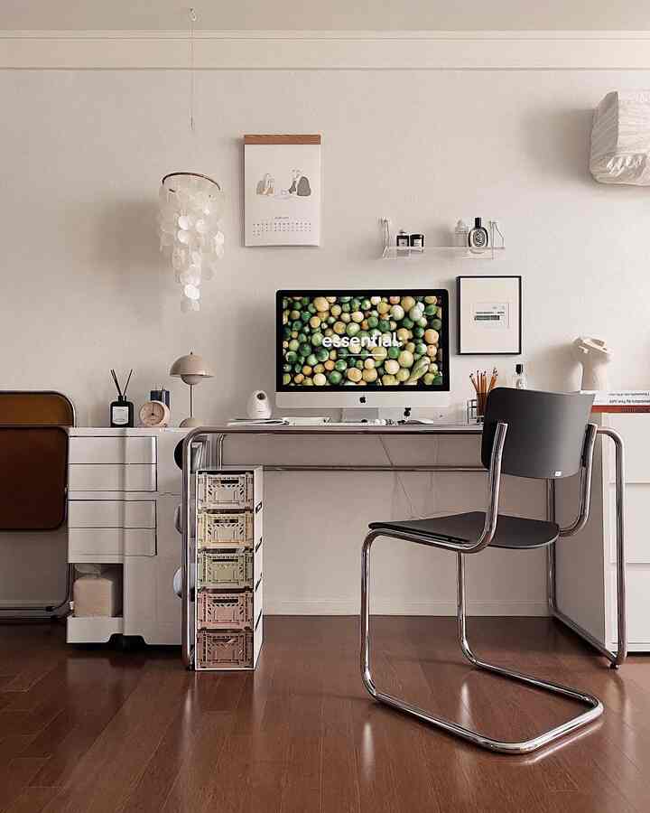 Minimal home office with white walls and brown wood flooring, featuring a desk with computer and folding storage boxes