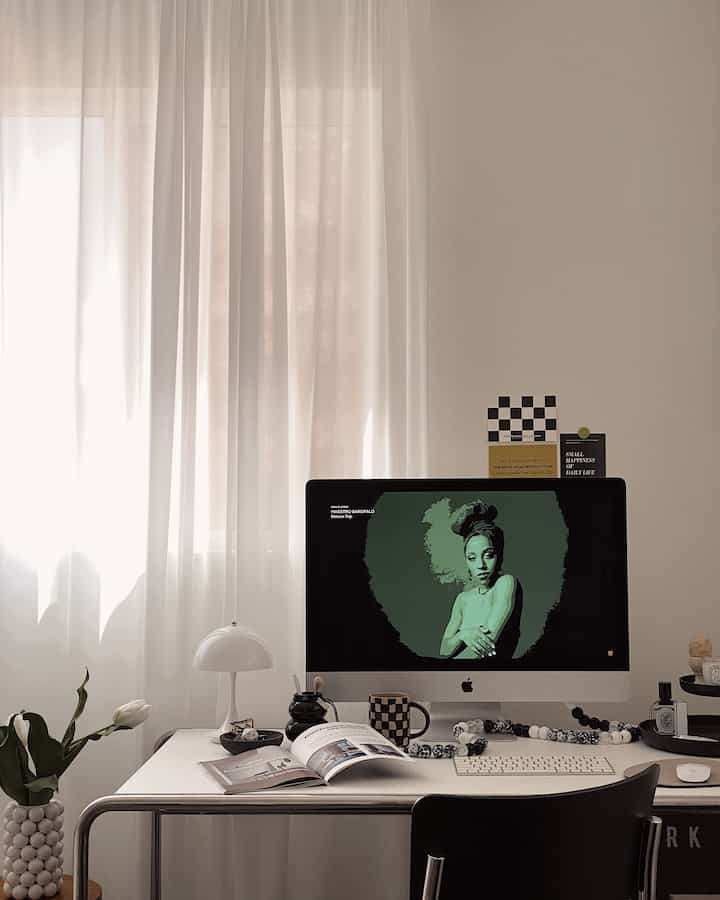 White and beige toned home office featuring a clean desk with iMac and table lamp, creating a focused work atmosphere