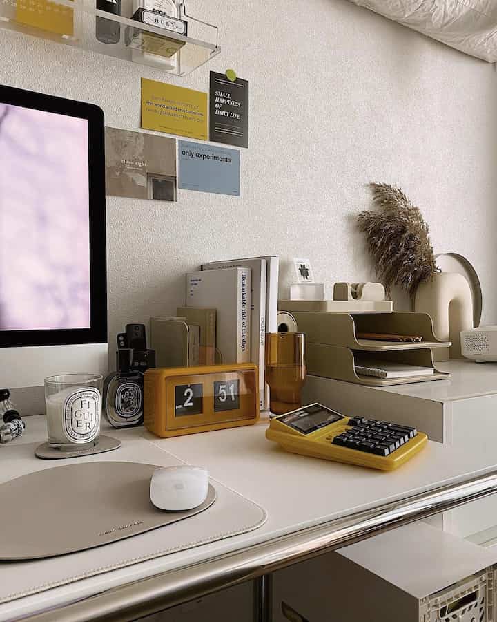 Natural beige-toned home office desk featuring clock, candle, calculator, and desk organizers with a tidy, cozy atmosphere