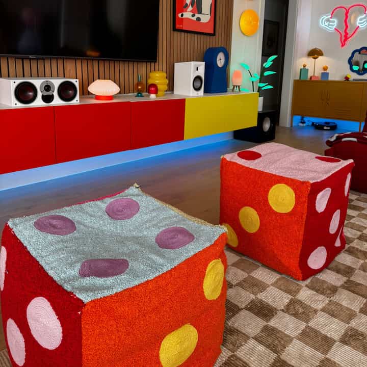 Living room in dominant red and yellow tones, featuring a media console and dice-shaped poufs with an Instagrammable vibe