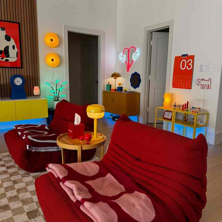 A bright and vibrant living room featuring red Togo sofas, yellow lighting fixtures, and colorful wall art creating a unique atmosphere