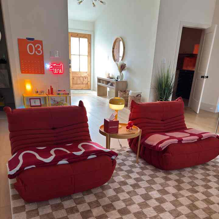 Natural-toned living room featuring two red lounge chairs and a table lamp with a cozy atmosphere