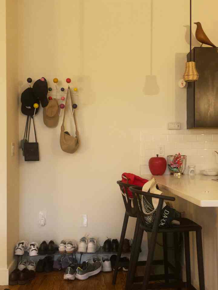 Beige walls and wood-tone floor define an entrance area with shoe rack, coat rack, and bar stools in a cozy setting