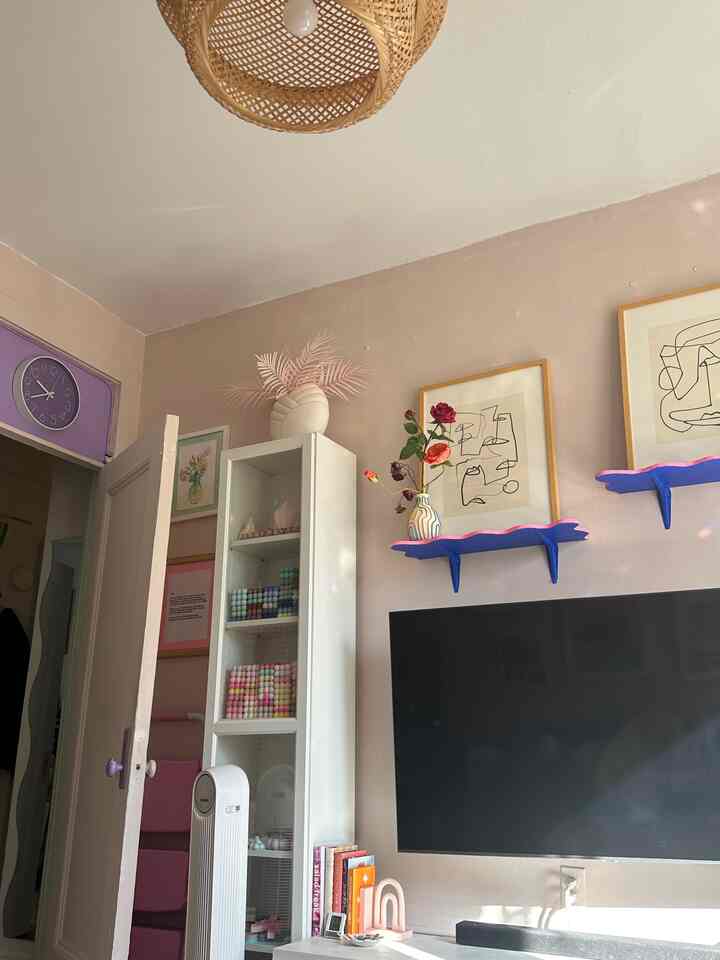 Pink and beige toned walls with white shelving and colorful decor in an Instagrammable apartment living room interior