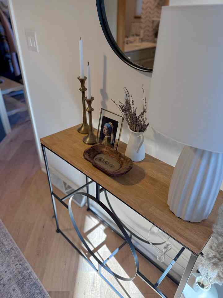 Natural wood tone console table with white walls, gold candle holders, and mirror in a modern entrance space