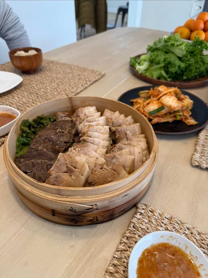 Natural wood-tone dining room featuring traditional bossam and kimchi on a rustic dining table with a cozy atmosphere