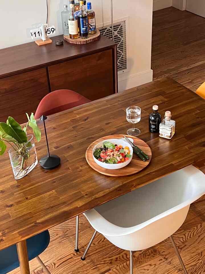 Cozy wood-toned dining room for four with white chairs, plant, and table lamp, featuring a neat lunch setup