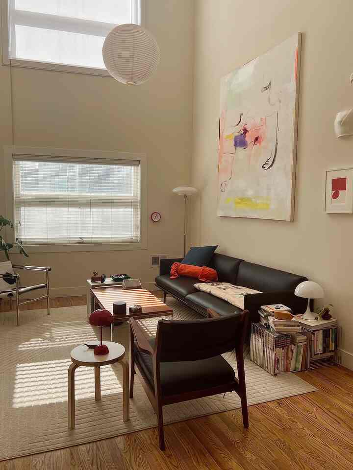Bright living room with white walls and brown wooden floor, featuring black sofa and armchairs, coffee table, and warm lighting