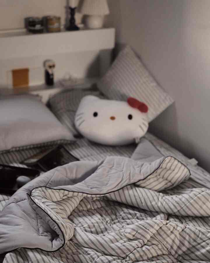 Small bedroom in white and gray tones, featuring neat bedding and a Hello Kitty stuffed pillow creating a cozy atmosphere