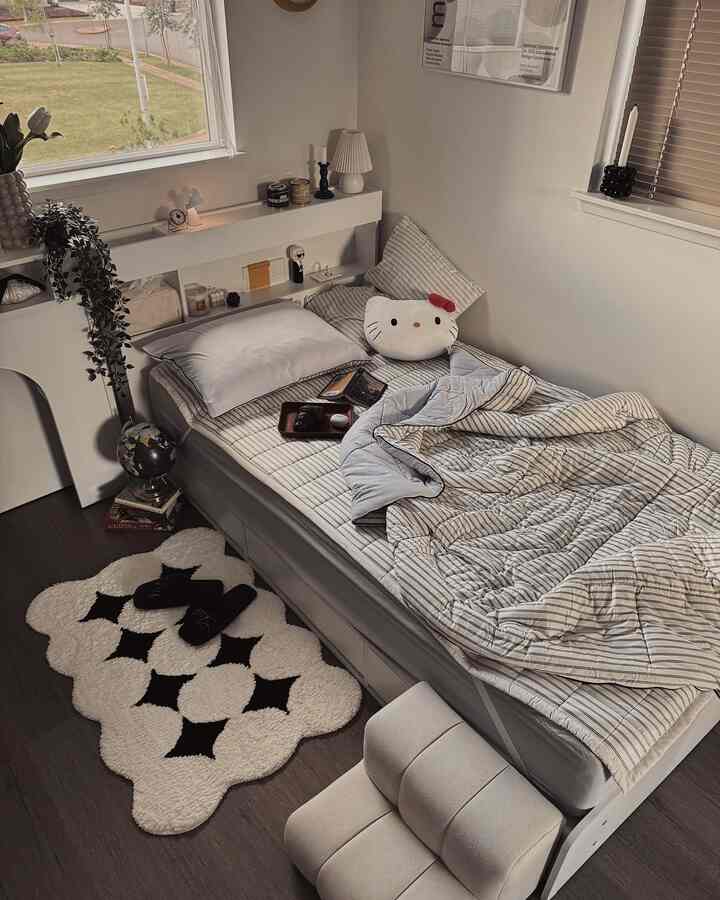 White and gray toned kids' bedroom featuring a bed with striped bedding, rug, plant, and cozy decor elements