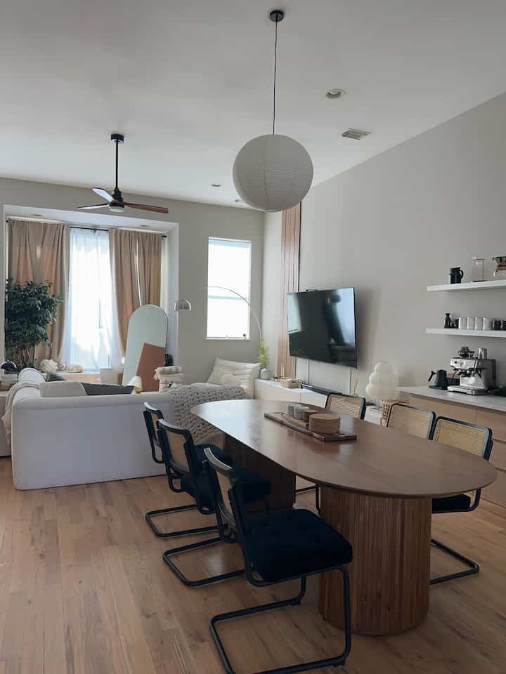 White walls and wood tone furniture blend in a dining and living room featuring minimal sofas and a coffee machine with a cozy atmosphere