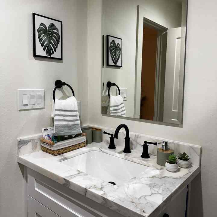 White and green toned bathroom sink area featuring a marble countertop, plants, and framed wall art creating a cozy interior