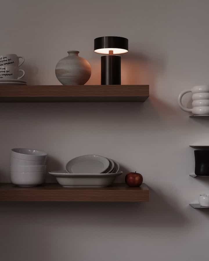 Modern dining room interior with brown wooden shelves, white ceramic tableware, and a black table lamp at center