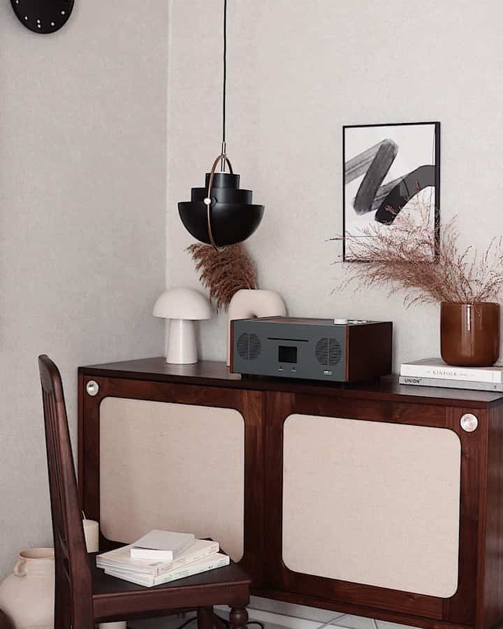 Brown and beige toned bedroom space featuring vintage sideboard, armchair, table lamp, and pendant light with a natural atmosphere