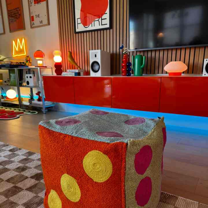 Bright red wall-mounted storage and various art objects with a colorful patterned pouf in a modern living room space