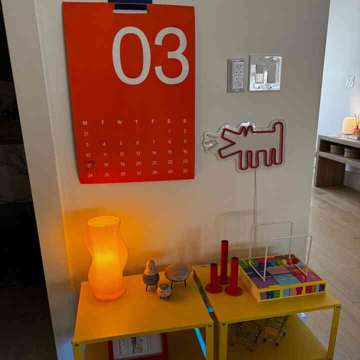 Yellow-toned living space corner featuring red wall calendar, wavy table lamp on side tables and colorful decorative objects with a vibrant vibe