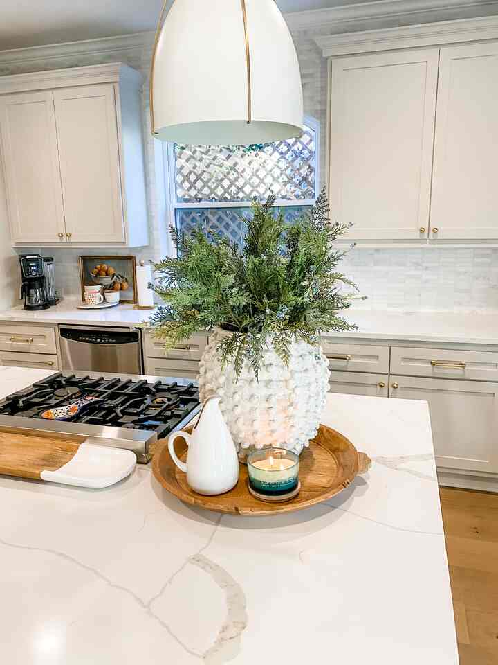 Bright white kitchen with wood tones, featuring a kitchen island centerpiece with greenery and a candle for cozy atmosphere