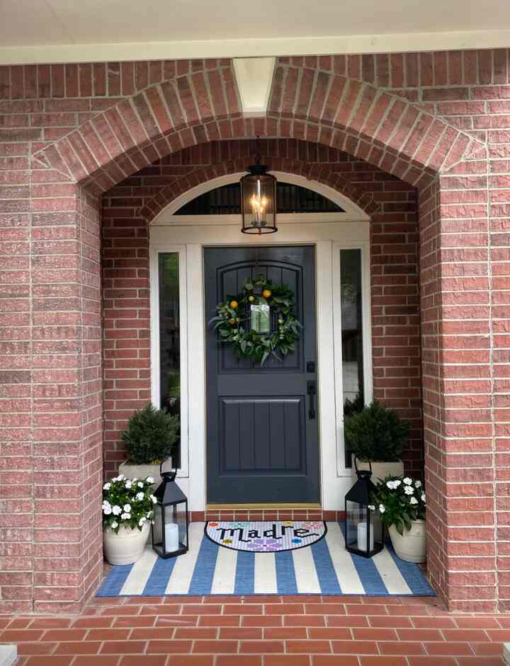 A natural spring porch space with a red brick arched entrance, blue door, and green wreath decoration