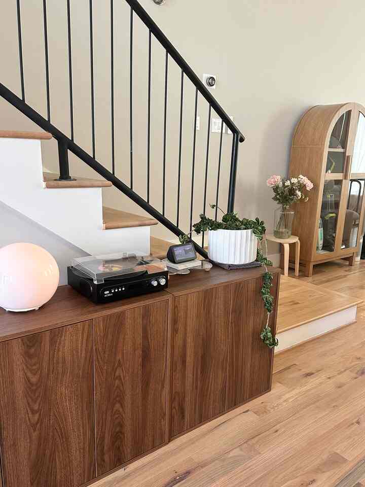 Natural wood tone space under stairs featuring wooden storage cabinet and green plant creating cozy atmosphere