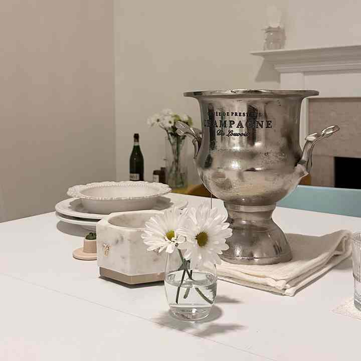 White-toned kitchen table featuring a vintage-style wine chiller and a vase of daisies in a tidy setting