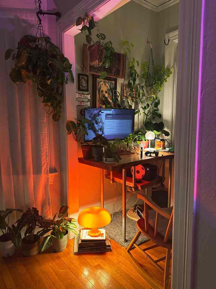Cozy home office with orange lighting, brown wood tones, abundant plants, and a desk setup