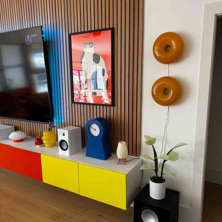 Living room with white walls and vibrant red and yellow cabinets, featuring a blue clock and cat art for a lively atmosphere