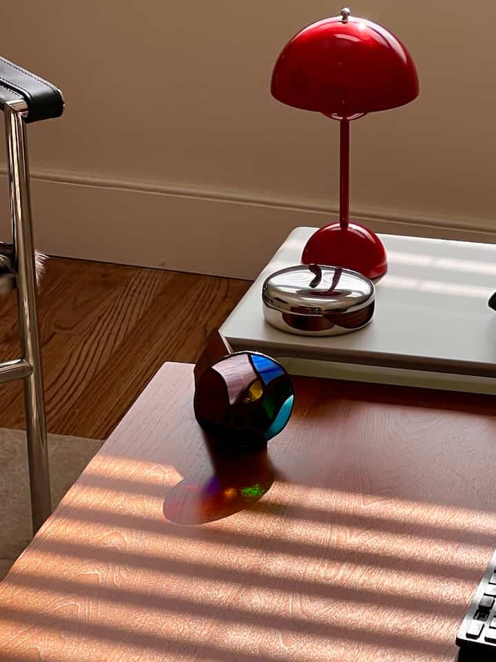 Cozy space with a red table lamp and a wood-tone table featuring a colorful kaleidoscope objet casting vibrant reflections