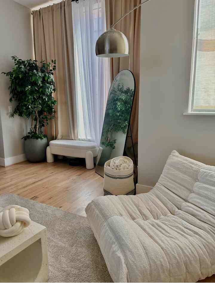 Beige and white toned living room featuring a large cushioned sofa, bench, and arched mirror with a cozy atmosphere