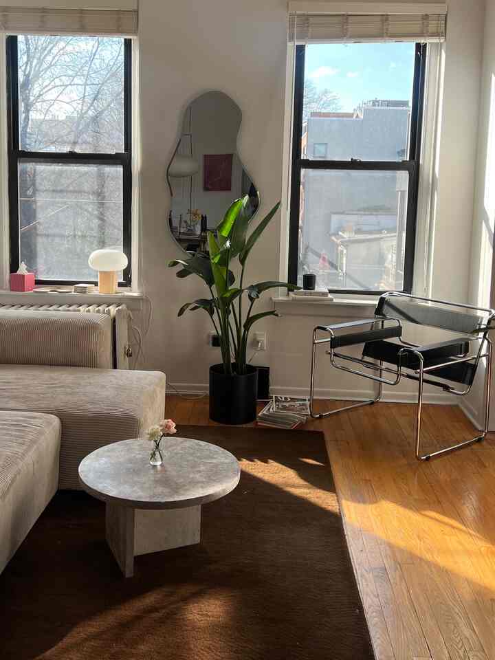A white living room with natural wood tones and dark brown rug, featuring a beige sofa and black metal armchair, creating a warm earthy atmosphere