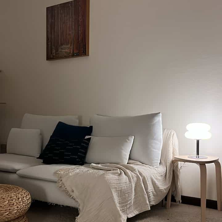 Warm beige and white toned living room featuring a white sofa and wooden side table with a glowing lamp, creating a cozy atmosphere