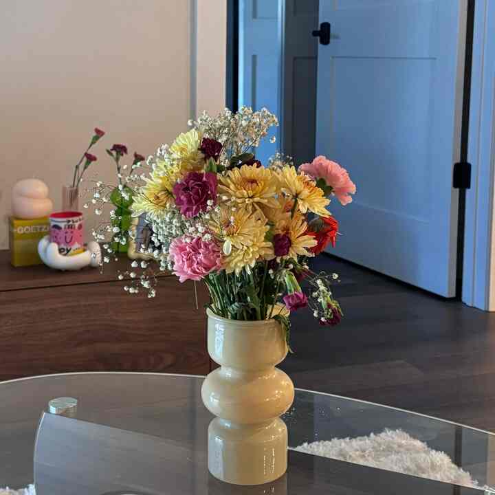 Natural beige-toned living room featuring a glass coffee table with a vase filled with colorful spring flowers, creating a cozy ambiance