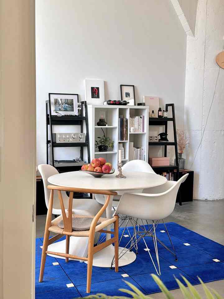 A white and wood tone dining room featuring a round dining table and chairs on a blue rug, with a clean and modern atmosphere