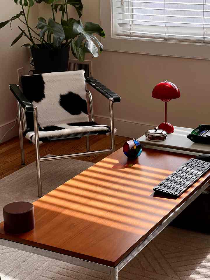 Cozy beige and wood-toned home office with a cowhide armchair and a red table lamp as focal points