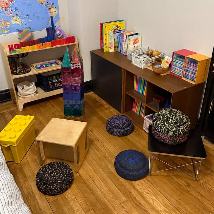 Brown wood-tone floor kids' room featuring toy storage, children's bookshelves, and scattered cushions