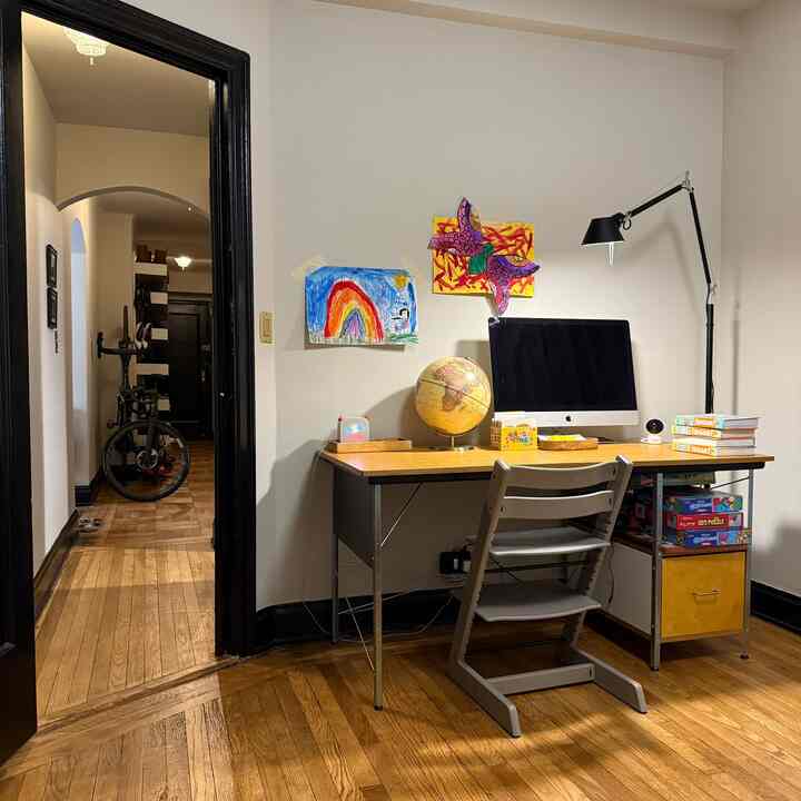 Natural wood tone and white-walled kids' room featuring a desk, children's artwork, and a floor lamp creating a warm study space