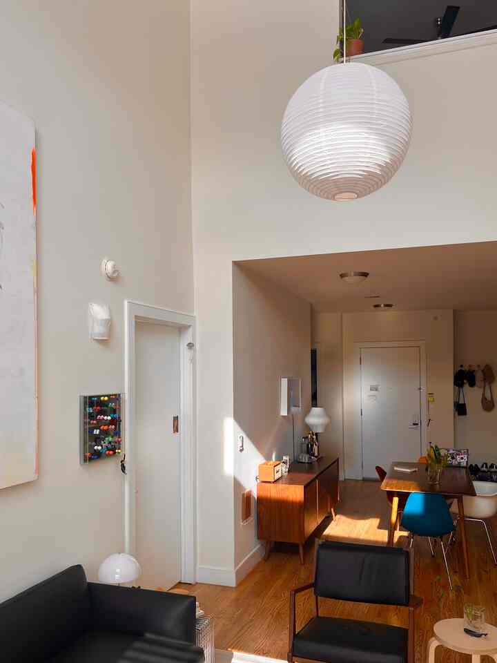 Modern studio apartment living and dining room with white walls and brown wood tones, featuring simple furniture and natural light