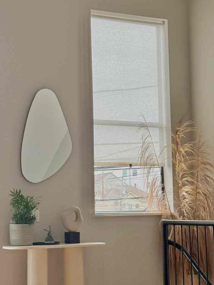 A natural beige and ivory-toned space featuring an asymmetrical mirror, blinds, and natural plants with a simple, serene vibe