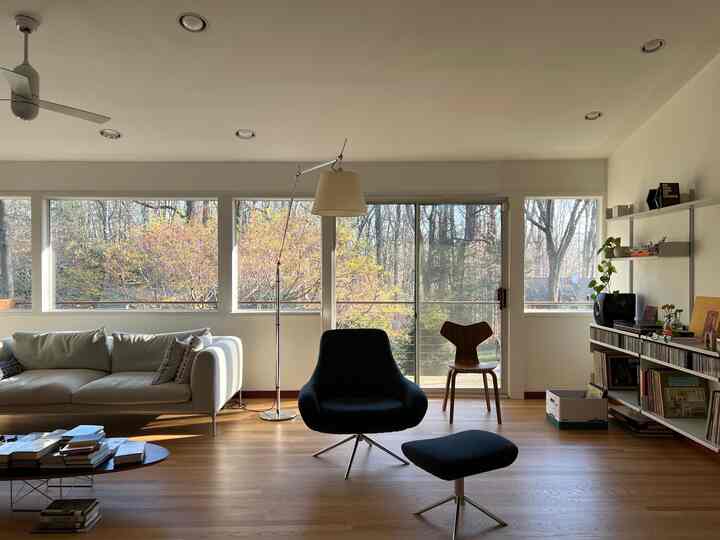 Bright living room with white walls and natural wood flooring, featuring a sofa, modern armchair, bookshelf, and floor lamp for a cozy atmosphere