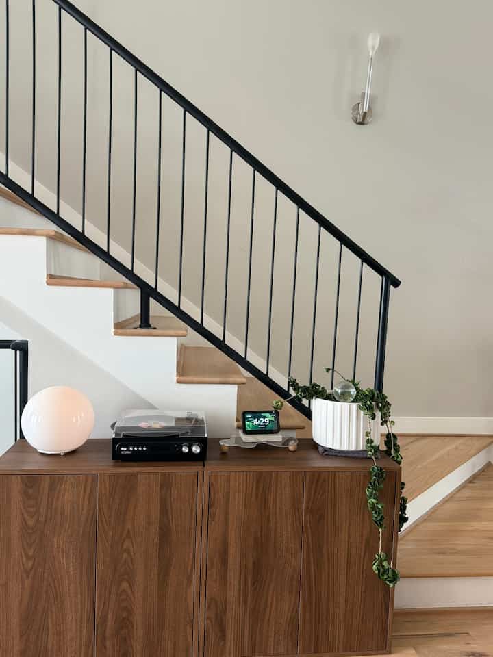 Compact space featuring wood-toned cabinet and black metal stairs, accented with a stylish lamp and cascading plant in a modern interior