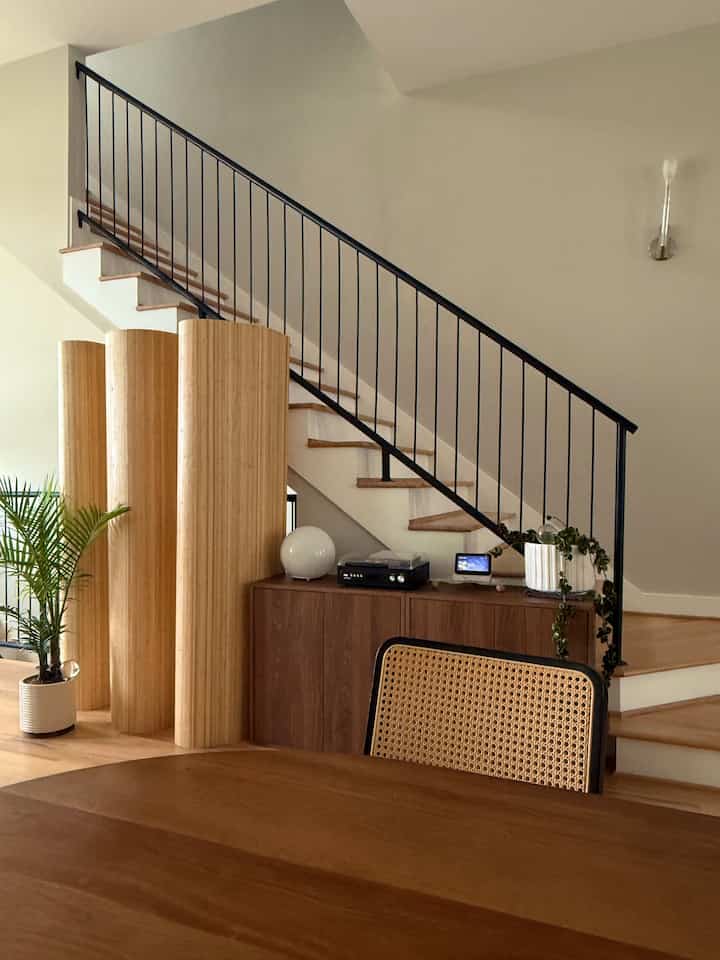 Natural wood tone dining table and stairs space featuring bamboo room divider with warm, calm atmosphere