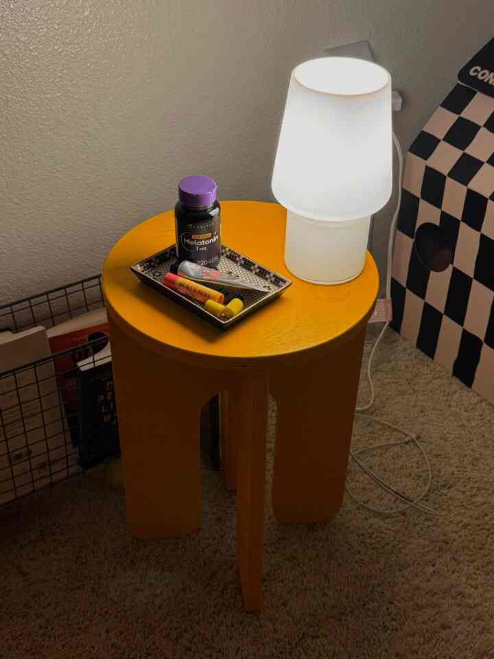 A bright yellow nightstand featuring a white table lamp and a tile pattern tray in a simple, organized bedroom corner
