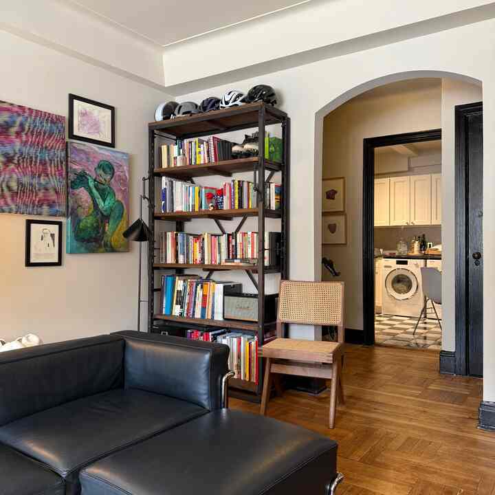 Living room with brown wood flooring and white walls featuring a black leather sofa and a tall bookshelf, creating a cozy atmosphere
