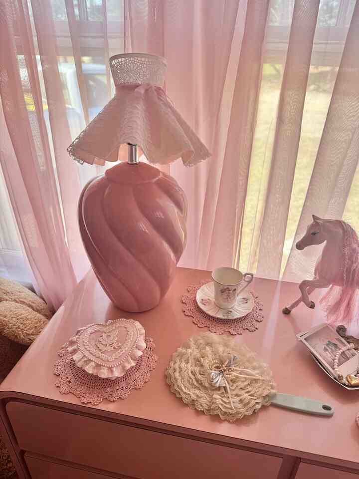 Pink-toned bedroom featuring a retro ceramic table lamp with lace lampshade and delicate vintage accessories in a shabby chic style