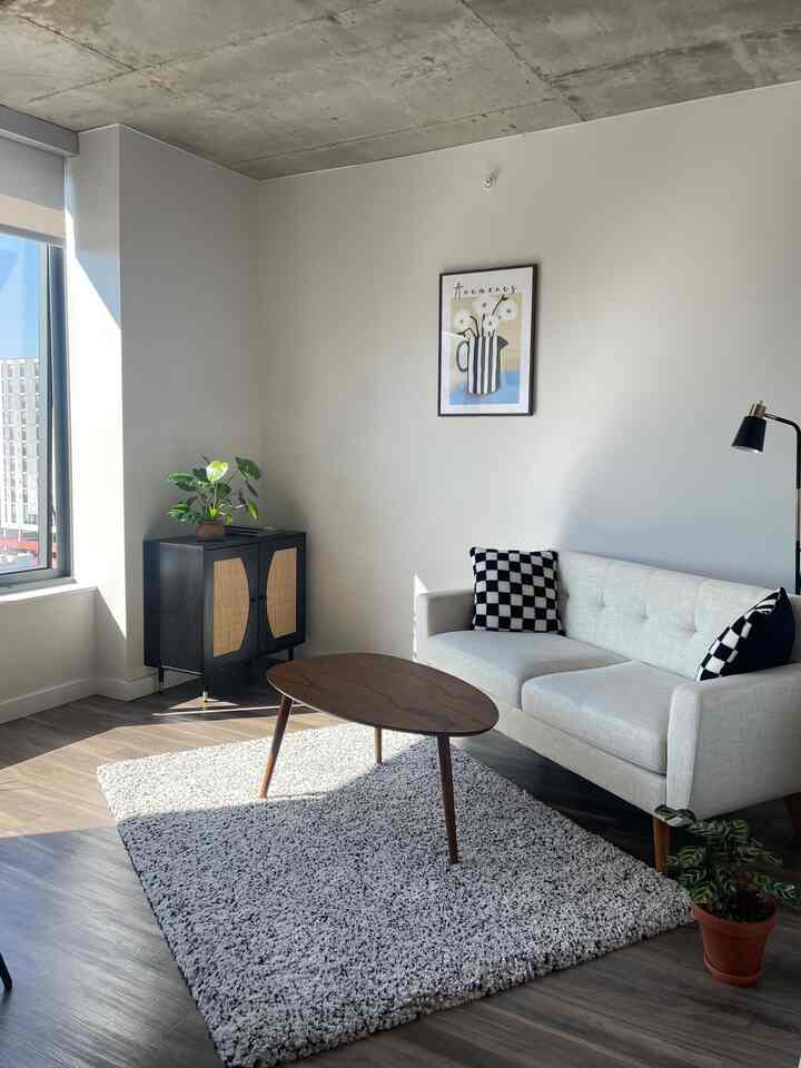 Bright white-walled studio apartment living room featuring natural wood tone furniture and a simple, cozy atmosphere