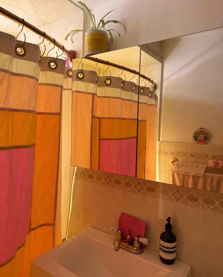 Orange-toned bathroom featuring a bright shower curtain and sink with warm ambiance