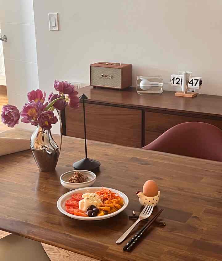 Warm brown wood and white background dining room featuring a wooden dining table with a single chair, vase, and table lamp in a natural modern style