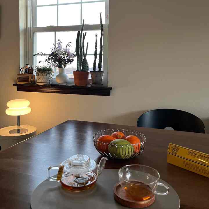 A white and brown toned dining room featuring a table lamp, plants on the windowsill, and a natural home cafe setup
