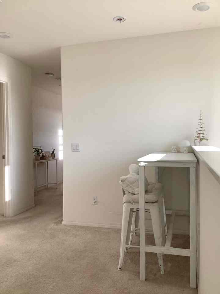 Bright white and beige toned narrow entrance featuring two bar stools and a small bar table with a simple and natural atmosphere